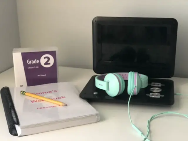 black dvd player, teal headphones, abeka academy workbook and Grade 2 Abeka Academy DVDs on white table