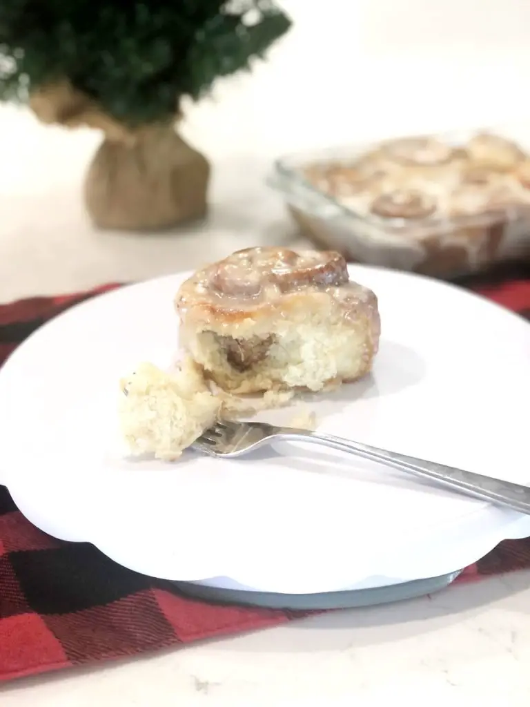 Baked cinnamon roll with a fork on a white plate