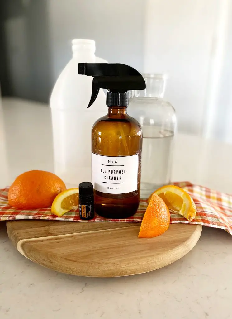 amber glass spray bottle, vinegar, water, orange slices and wild orange essential oil on wooden cutting board