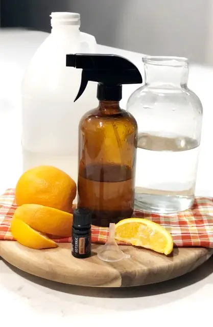 amber glass spray bottle, orange slices, glass jar with water, vinegar and wild orange essential oil on wooden cutting board