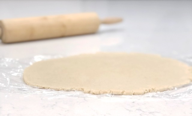 wooden rolling pin and rolled out sugar cookie dough on white counter top