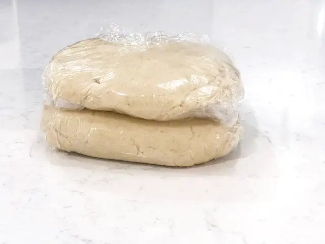 two flat discs of cookie dough wrapped in plastic wrap on white counter top