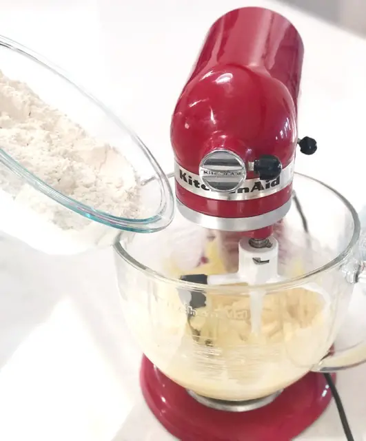 Red kitchen aid mixer with glass bowl filled with cookie dough