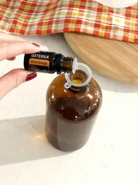 woman's hand pouring wild orange essential oil into amber glass spray bottle