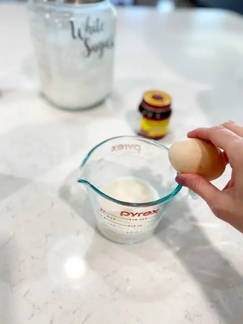 cracking an egg into a measuring cup filled with almond milk