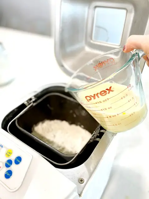 measuring cup with milk, water and beaten egg being poured into bread machine