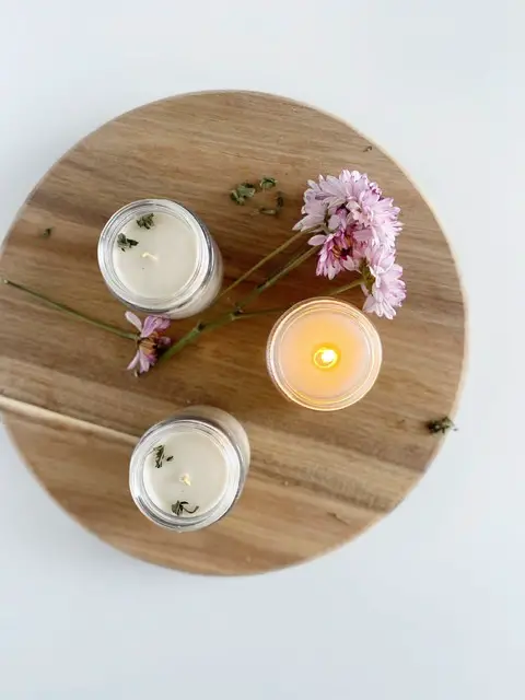 three beeswax candles on wooden cutting board with purple flower, one lit