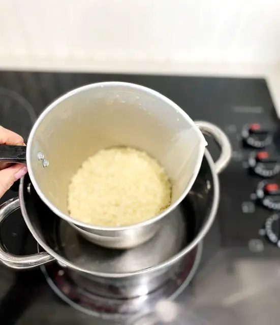 organic beeswax pellets in metal pitcher on doubler on stove