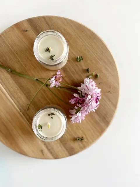 Two organic beeswax candles on cutting board with purple flowers, top view