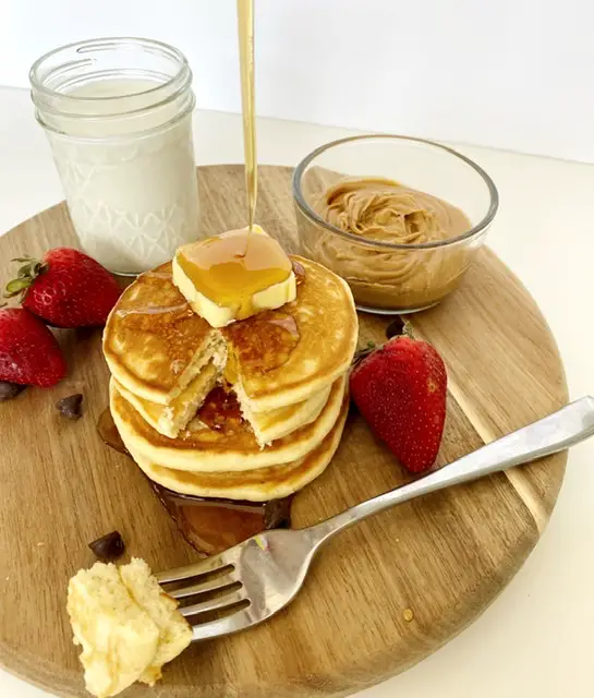 stack of easy and fluffy gluten free pancakes with strawberries, glass of milk, chocolate chips and peanut butter 