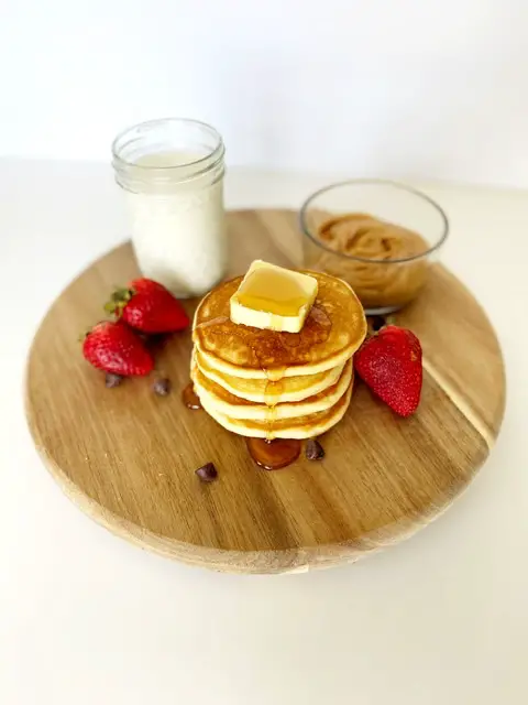 stack of easy and fluffy gluten free pancakes with strawberries, glass of milk, chocolate chips and peanut butter 