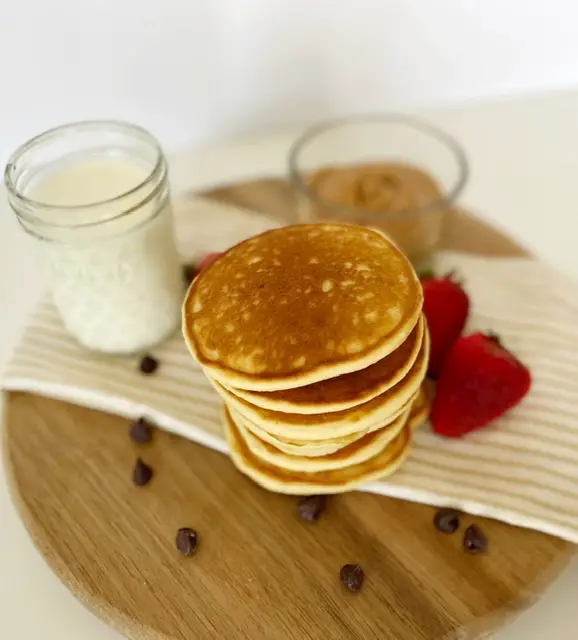 stack of easy and fluffy gluten free pancakes with strawberries, glass of milk, chocolate chips and peanut butter 