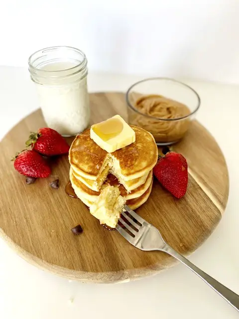 stack of easy and fluffy gluten free pancakes with strawberries, glass of milk, chocolate chips and peanut butter 