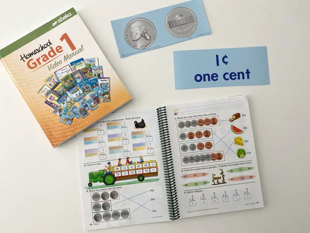 Abeka Arithmetic grade 1teacher workbook and video manual on white table with abeka money manipulatives