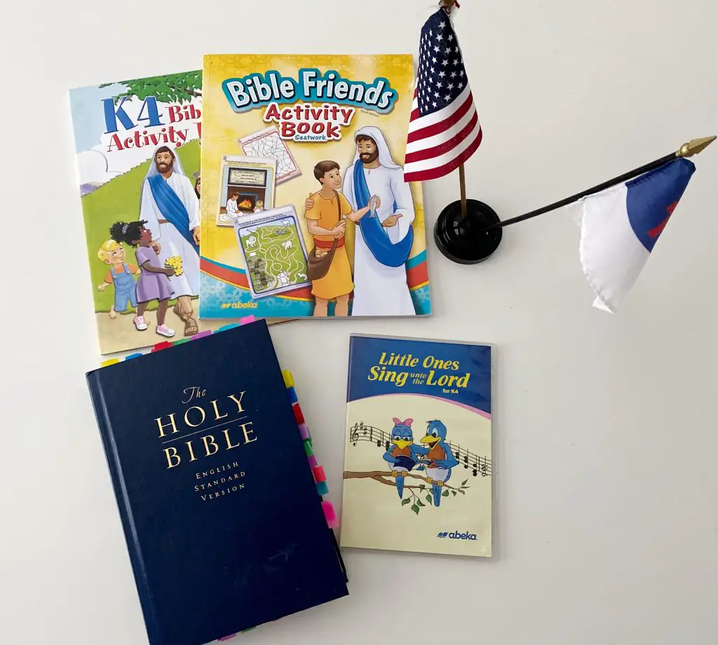 Abeka K4 & K5 Bible Curriculum, American Flag, Christian Flag, Holy Bible and Little Ones Sing unto the Lord CD on white table 