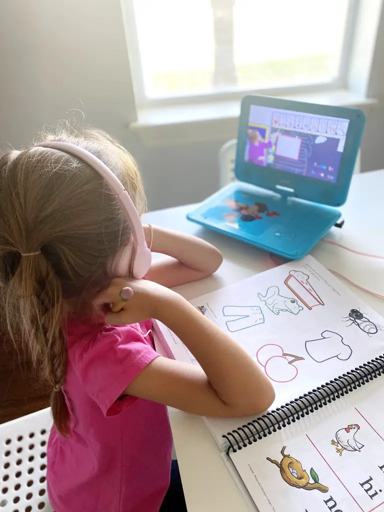 Girl with pink headphones and turqoise dvd player doing homeschool lesson with abeka academy 