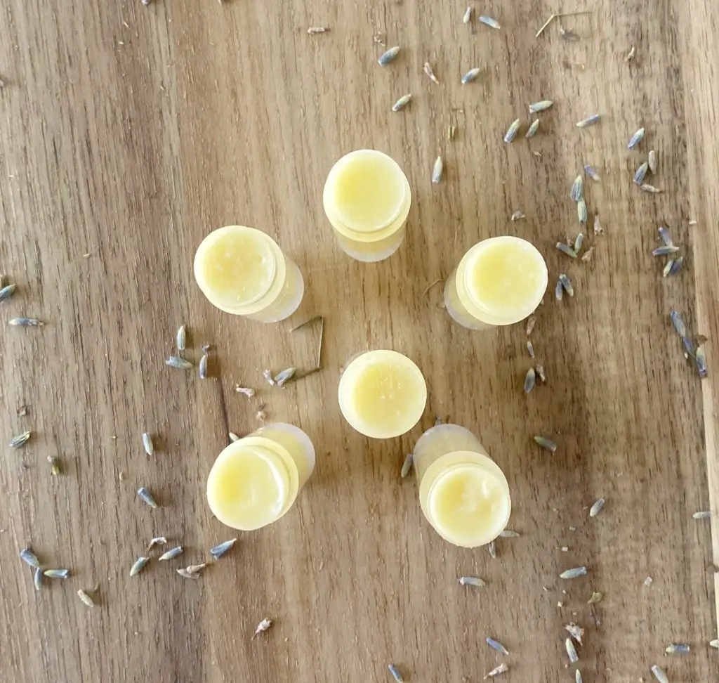 6 tubes of homemade beeswax lip balm with butcher block and lavender petals 