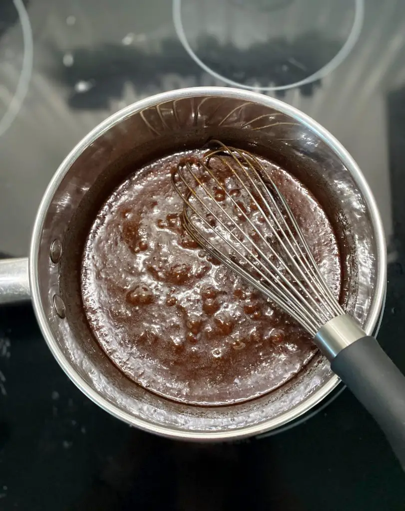 sugar and cocoa bubbling in stainless steel pot with whisk 