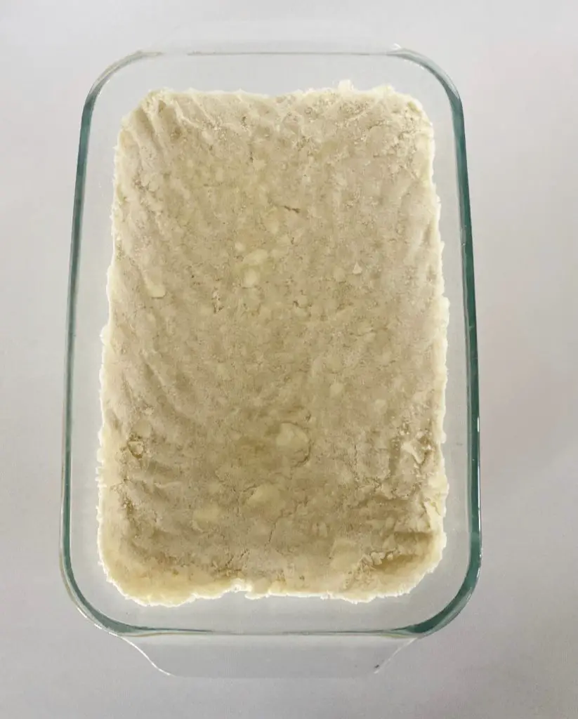 Glass dish with gluten free yellow cake mix and cold butter pressed into bottom 